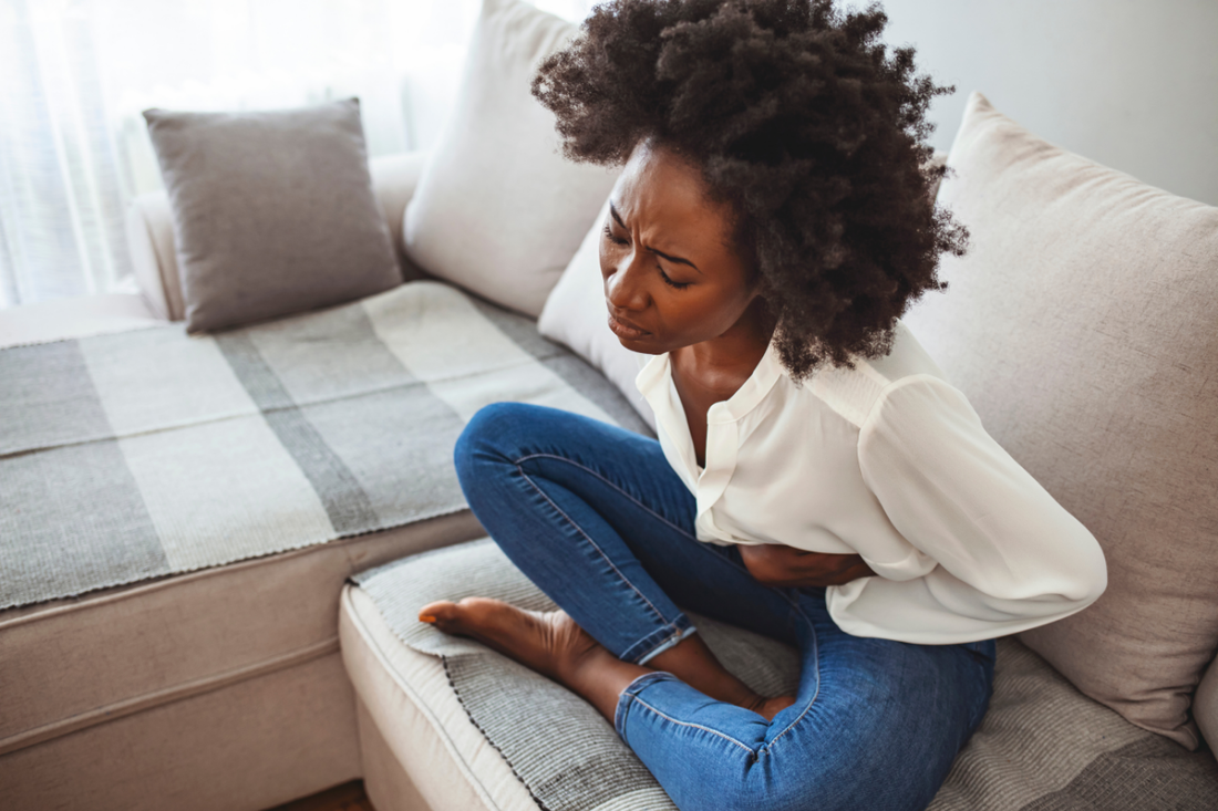 Black woman sitting on a couch having menstrual cramps and holding her abdomen in pain.