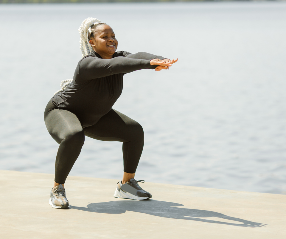 Black woman squatting in front of a lake.