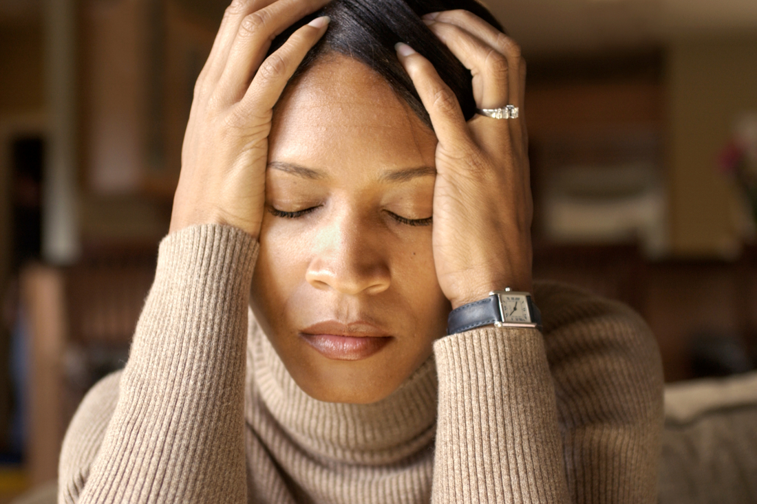 Close-up of stressed woman with her eyes closed and her hands holding the sides of her head.