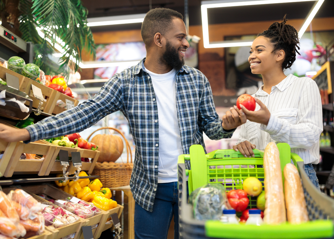 Smiling Black couple in grocery store shopping for fruits and vegetables.