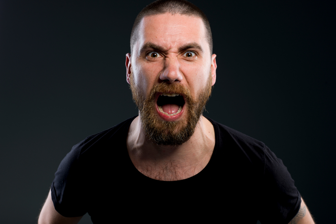 White bearded man in a black shirt yelling in front of a black background.
