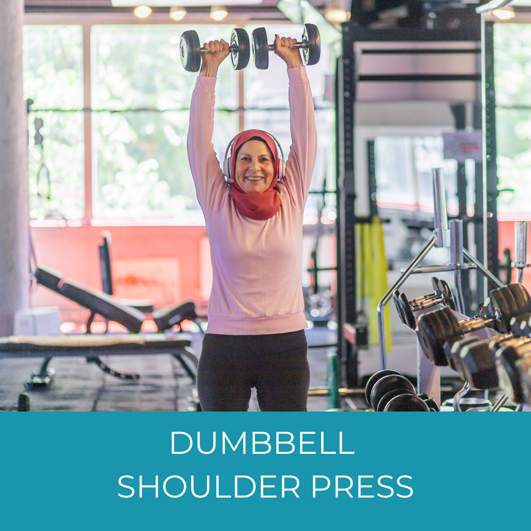 smiling woman in hijab doing dumbbell shoulder presses at the gym