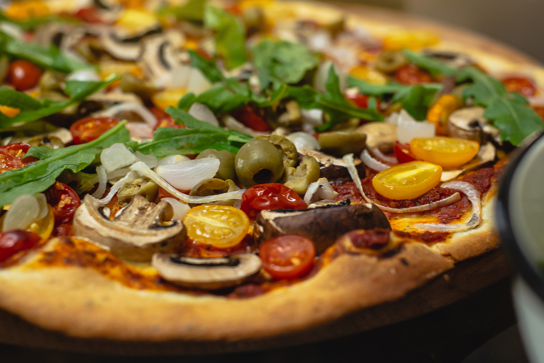 Vegan substitutes - plant-based pizza with mushrooms, cherry tomatoes, onion, and arugula.